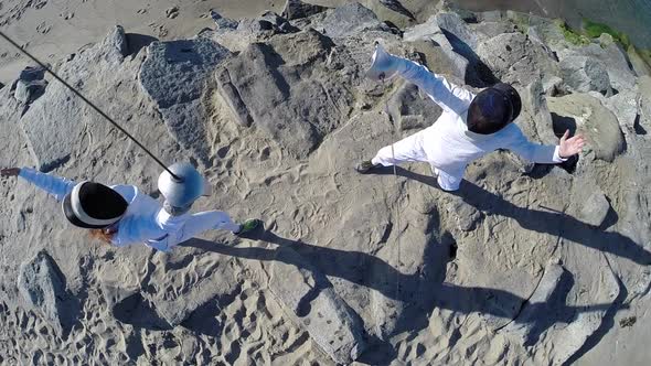 A man and woman fencing on the beach. alt
