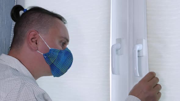 Adult Sad Man in Face Medical Mask Looks Through Window