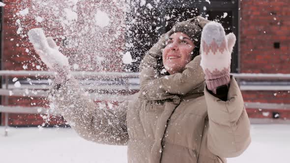 Happy Young Woman Throwing Snow on City Street alt