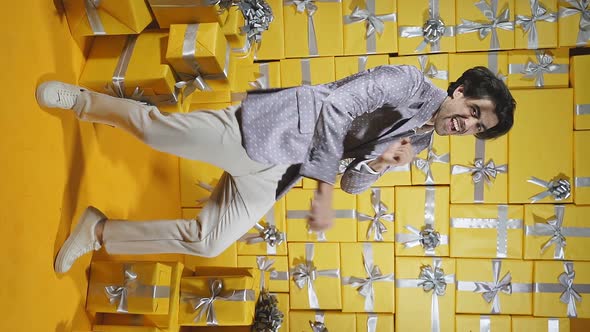 A Cheerful Young Man in an Elegant Gray Suit is Dancing in a Room Full of Gift Boxes Posing for the