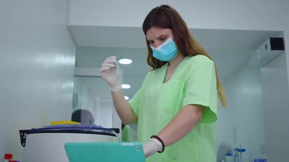 Side View Focused Smart Laboratory Assistant Checking Test Tube Entering Data in Digital Tablet alt