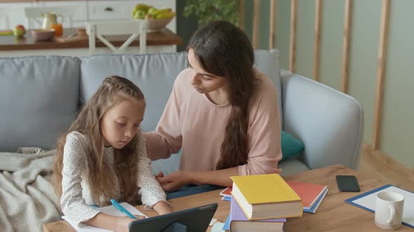 A Lovely Mother Helps To Her Cheerful Daughter Do Homework. Girl Takes a Remotely Education alt