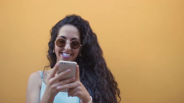 Happy Young Hipster Woman with Sunglasses Texting on Smartphone