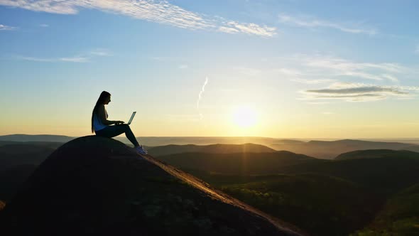Aerial Shots of a Silhouette of a Young Freelance Woman Working on a Laptop Sitting on Top of a