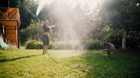 A Happy Young Woman Having Fun and Pouring Water on Herself From a Hose alt
