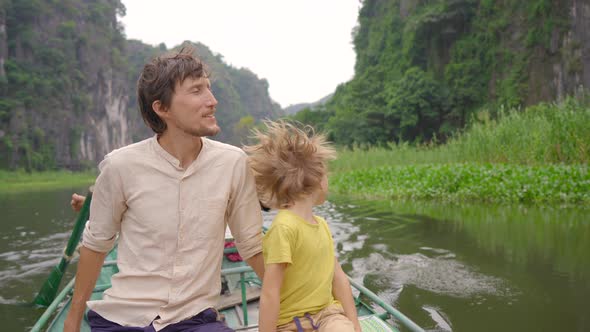 A Young Man and His Son on a Boat Having a River Trip Among Spectacular Limestone Rocks in Ninh Binh alt