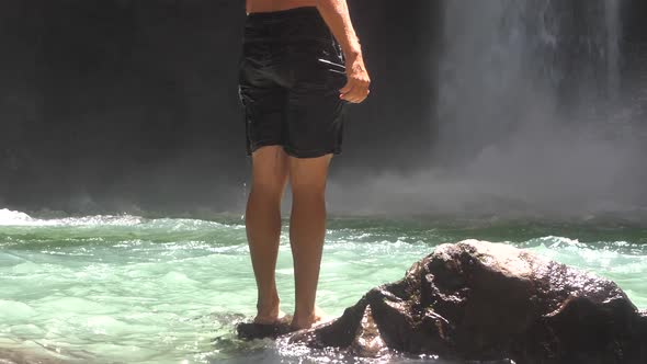 Half View of a Man Standing on a Rock Near and in Front of a Waterfall