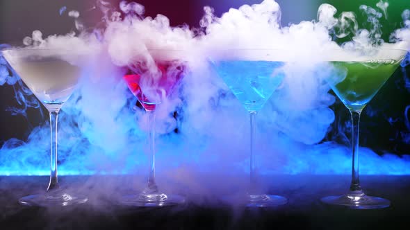 Colorful drinks with dry ice smoke effect. Bartender show and prepared cocktails on bar counter.