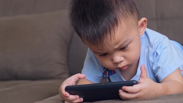 Little Boy Laying On A Sofa Watching On Mobile Phone alt