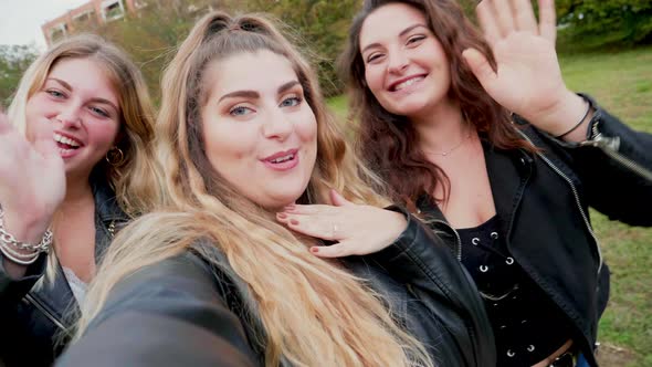 Three young women smiling and waving to camera in park, Italy
