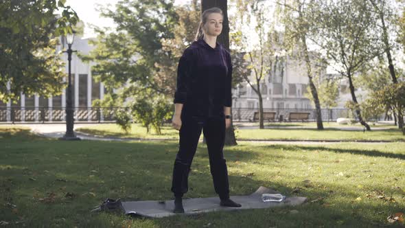 Wide Shot of Concentrated Young Sportswoman Doing Squats Outdoors on Sunny Summer Day alt