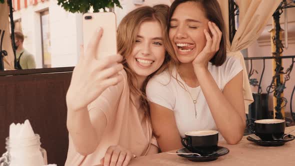 Two young beautiful smiling hipster girls chatting in cafe