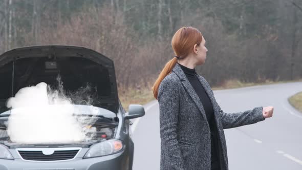 A Woman Stands By the Road Near a Broken Car