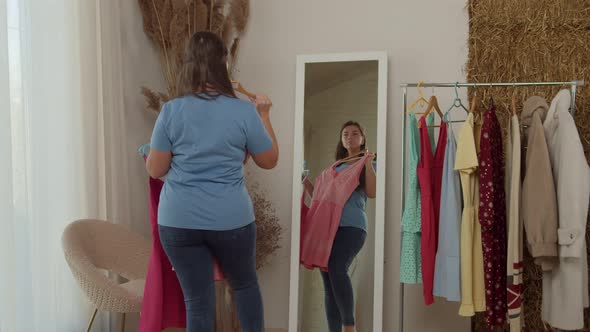 Plussize Woman Comparing Dresses Standing in Front of Mirror Indoors alt