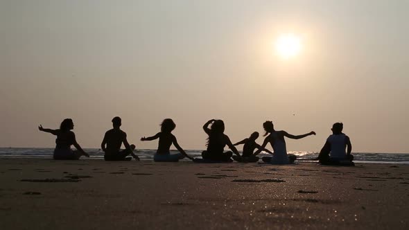 People practicing yoga at a sandy beach in Goa at sunset. alt