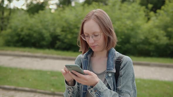 Student Woman in Glasses Denim Jacket Chatting Online Uses Smartphone Social Media