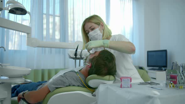 Dentist in Mask Checks the Patients Teeth alt