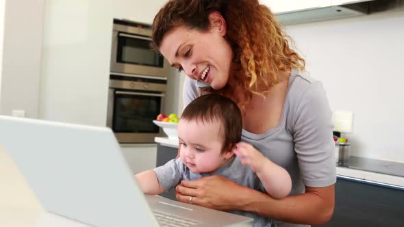 Mother Sitting with Baby Boy on Lap Using Laptop and Talking on Phone alt