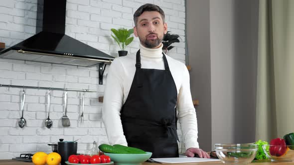 Man chef food blogger in apron greets teaches online videocall webcam in kitchen alt