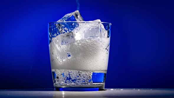 Glass of Water with Ice on a Dark Blue Background alt