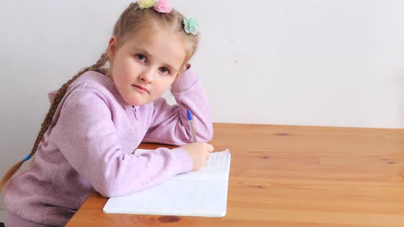 Little Girl Learns Lessons at Home Sitting at the Table