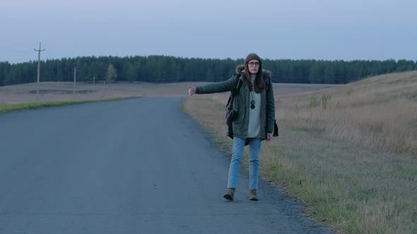 Young Beautiful Woman Hitchhiking Standing on the Road with a Backpack alt