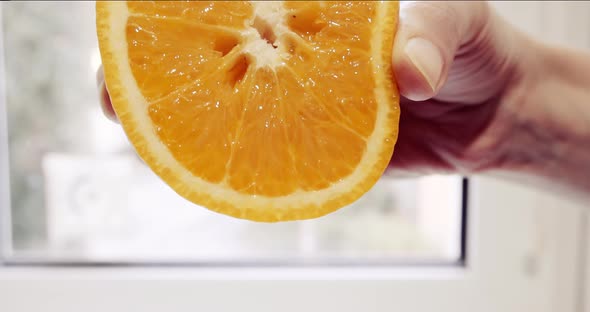 The woman's hand squeezes a juicy orange and juice flows out of it