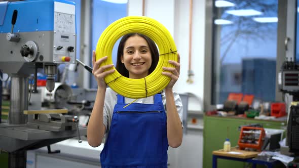 Smiling apprentice looking through yellow role of cables in factory alt