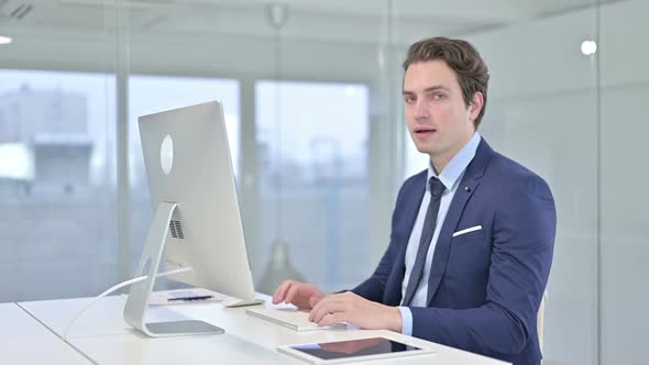 Cheerful Young Businessman Pointing Finger at Camera in Office  alt