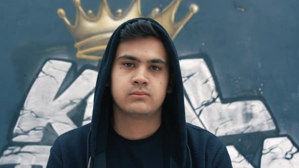 Young man looking at camera in front of graffiti wall. alt