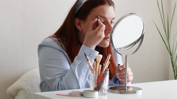 Woman Doing Makeup Put Cosmetics on Face Looking in Mirror at Home
