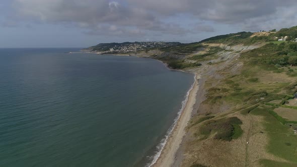 Aerial on the edge of Charmouth tracking forwards along the coast towards Lyme Regis. Glorious Juras alt