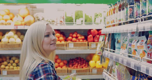 Attractive Woman is Walking Near the Supermarket Shelf and Selects the Products alt