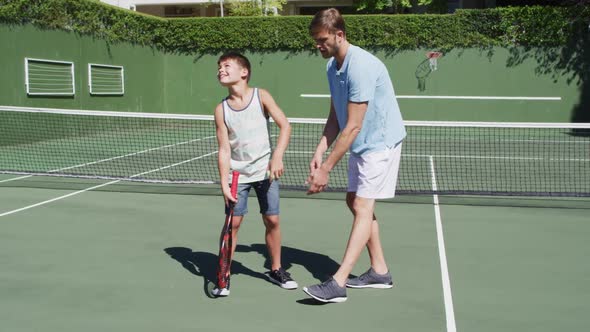 Caucasian father teaching his son to play tennis at tennis court on a bright sunny day alt