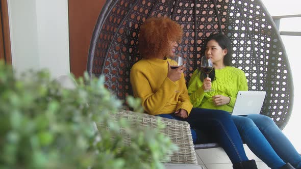 Two Woman Gossiping in the Swing. Lesbian Couple Relaxing and Drinking Red Wine alt