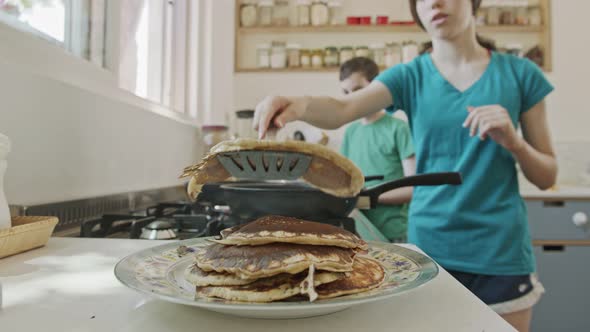 Young kids preparing pancakes in the kitchen using a frying pan alt