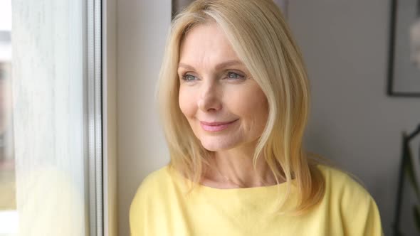 Charming Elderly Woman Stands with Cup of Morning Coffee Looks at the Camera and Smiles alt
