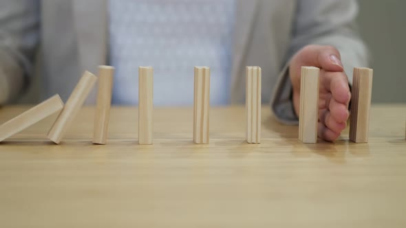 Businessperson Hand Stopping Colorful Blocks From Falling on Table in Office alt
