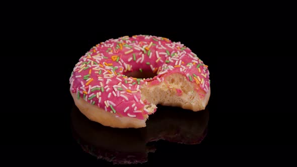 Donut with pink icing and colorful sprinkle rotating on a black background. 