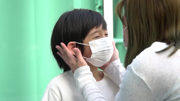 Asian Mother Puts A Safety Mask On Her Son Face alt