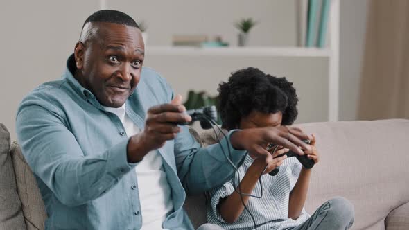 Mature African American Father with Little Daughter Playing Video Games on Console Use Joystick alt