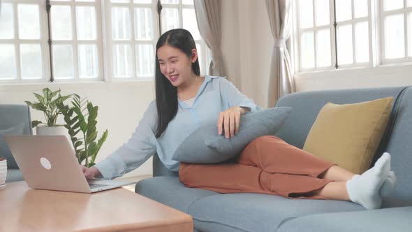 Asian Female Use Laptop Computer In Living Room While Lying On Sofa alt
