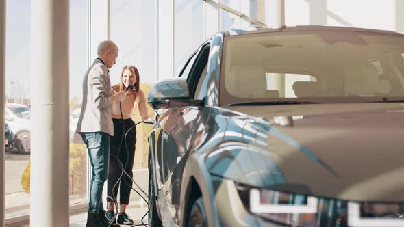 Two Happy Young Beautiful Women are Charging an Electric Car for the First Time alt