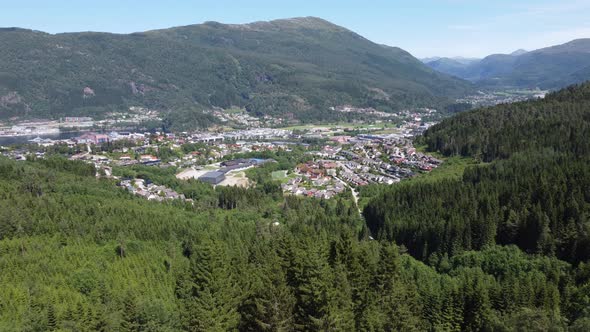 Panoramic view over Førde city from a distance - Rotating aerial behind lush forest with parallax ef alt