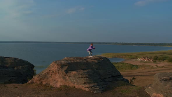 A Girl is Doing Fitness on a Hill on the Lake Shore