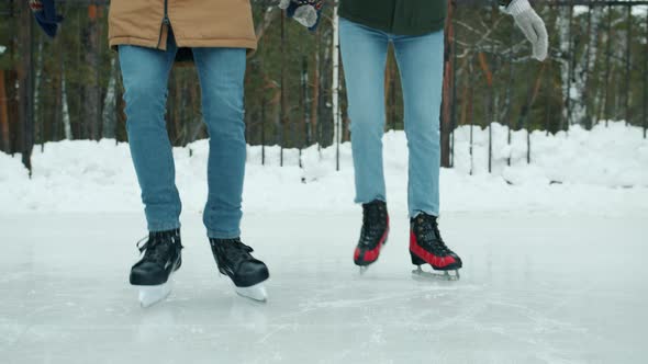 Low Shot of Couple Man and Woman Ice-skating in Park Wearing Jeans and Blades alt