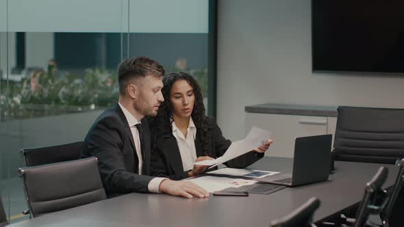 Two Coworkers Reading Papers Discussing Work Project Sitting In Office alt