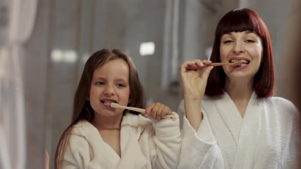 Kid Girl and Mom Brush Their Teeth and Look at the Camera alt
