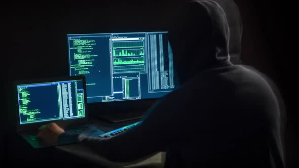 hacker in front of two monitors with computer code