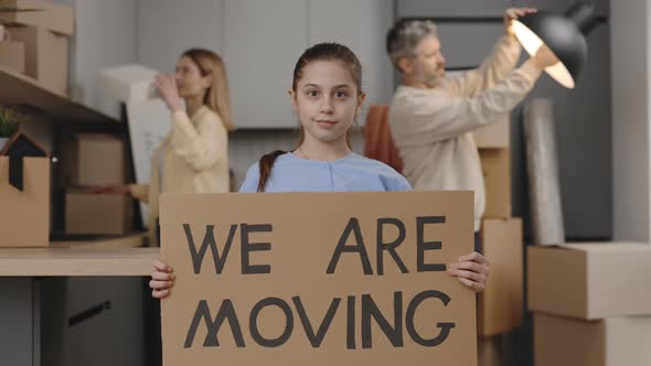 Slow Motion Portrait of Daugther Holding Paper Banner We are Moving Standing in New Home Smiling alt